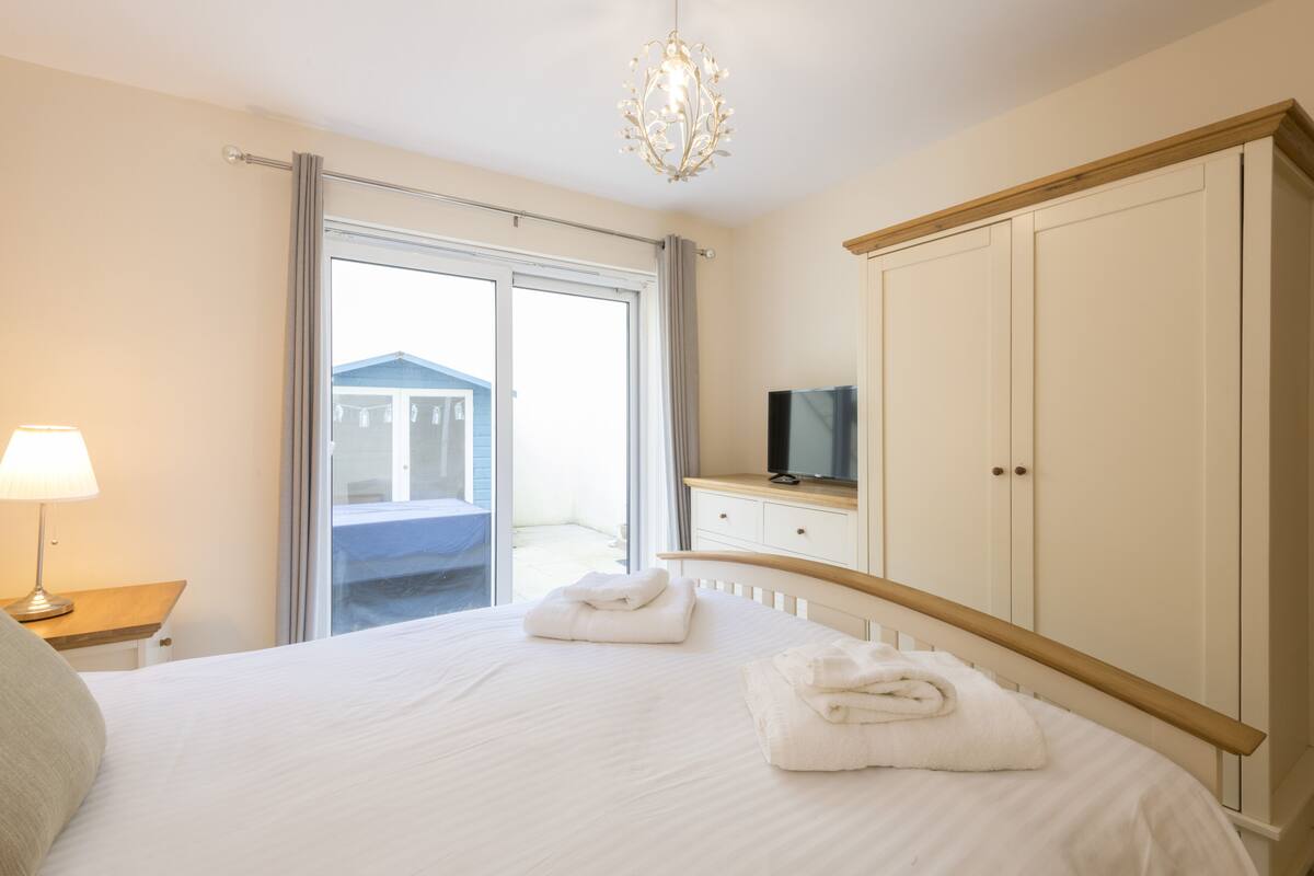 Une chambre à coucher avec un lit, un téléviseur posé sur une commode et un balcon visible par la fenêtre.