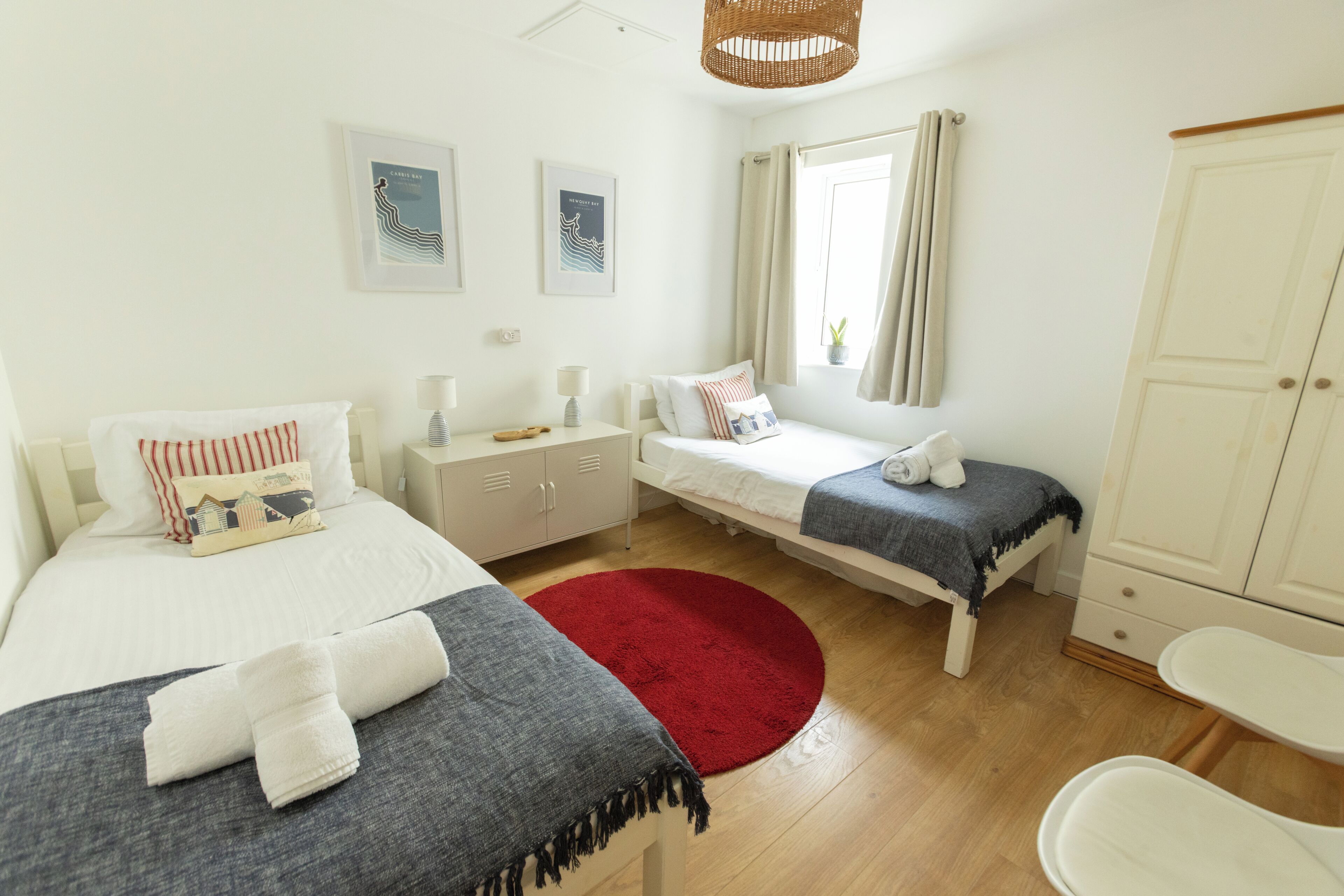 Une chambre avec deux lits, un tapis rouge, une armoire blanche et une fenêtre avec des rideaux.