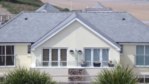A building with a sloped roof, large windows, and a balcony with potted plants. - The Beach House & Porth  Sands Apartments (Newquay)