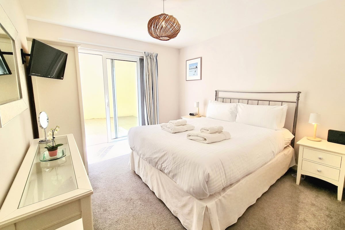 Une chambre d’hôtel comprenant un lit, une table de chevet avec une lampe, un téléviseur fixé au mur et une porte-fenêtre coulissante donnant sur un espace extérieur.