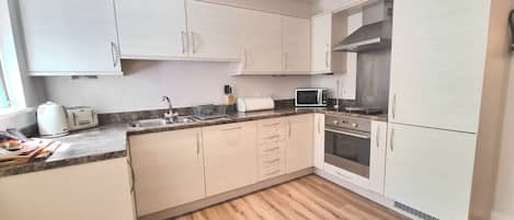 A modern kitchen with light-colored cabinets, a granite countertop, a built-in oven, and a microwave.