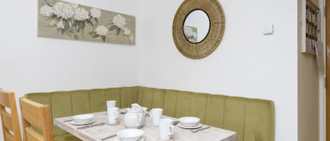 A dining area with a wooden table set for four, a green cushioned bench, and a wall-mounted mirror.