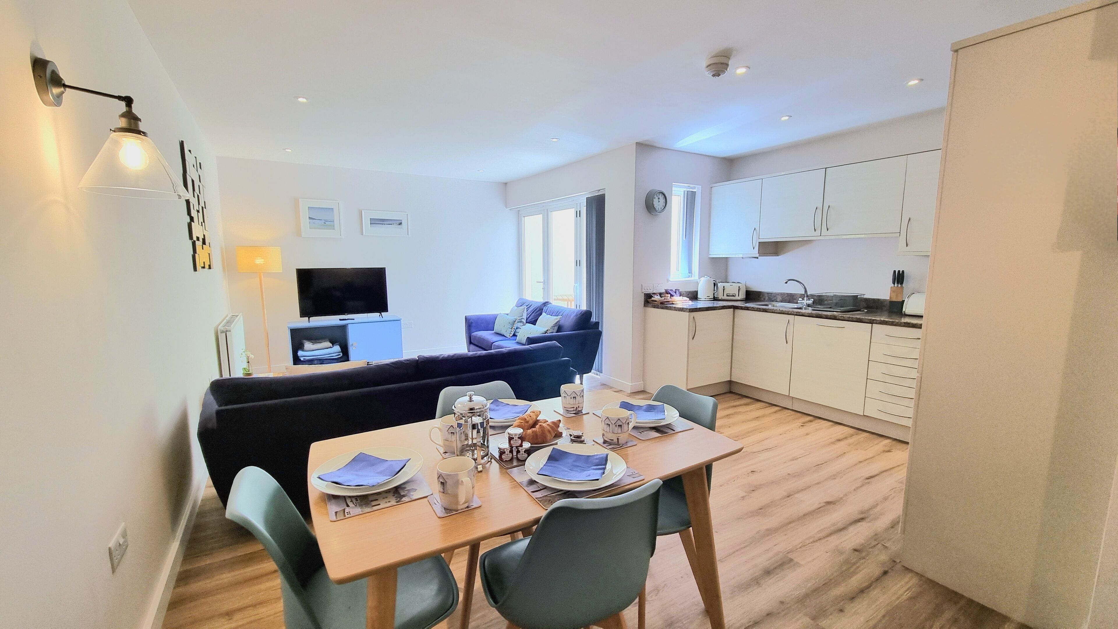 A modern apartment with a dining area, a living room with a sofa, and a kitchen.
