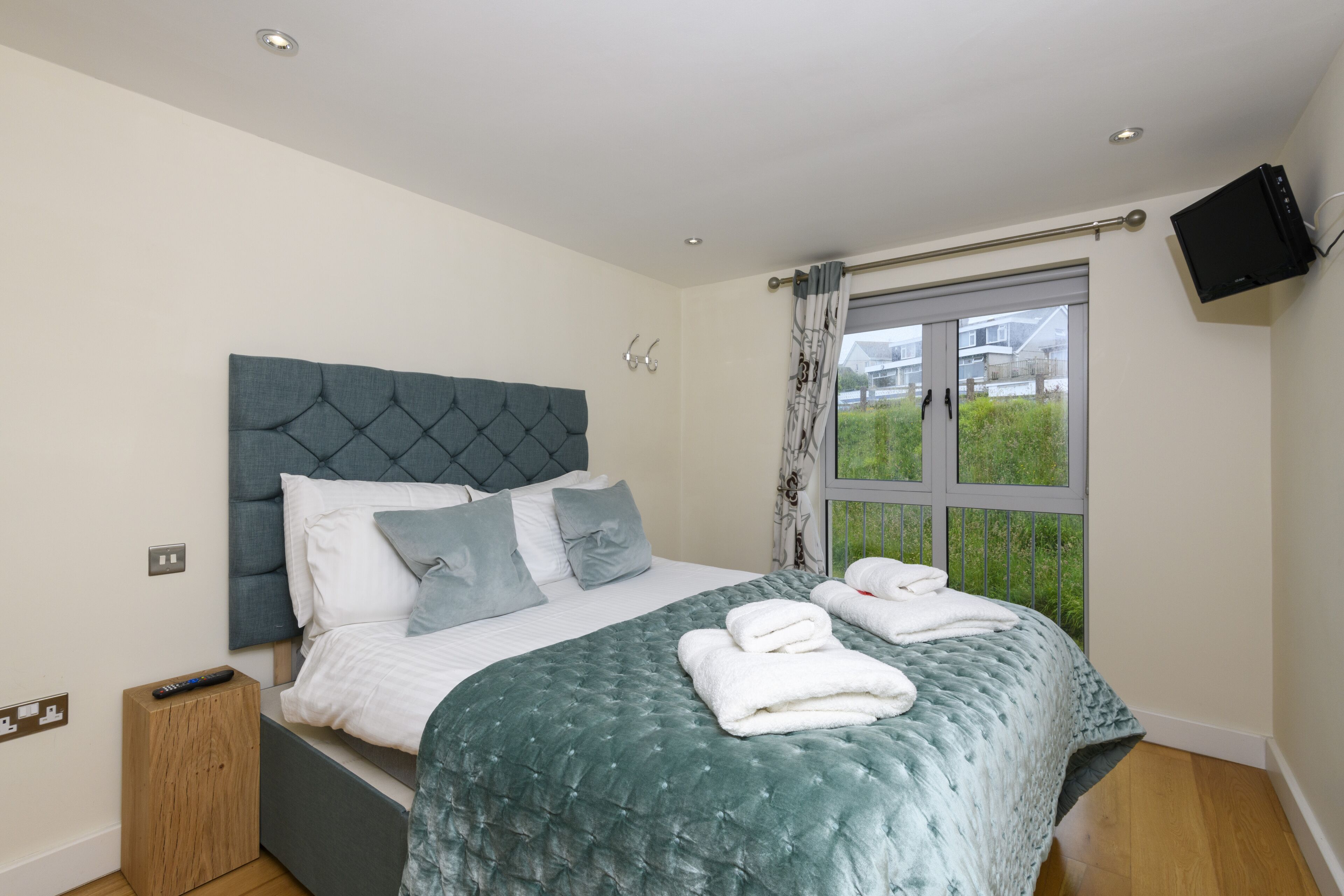 A bedroom with a large bed, a television mounted on the wall, and a window with curtains.