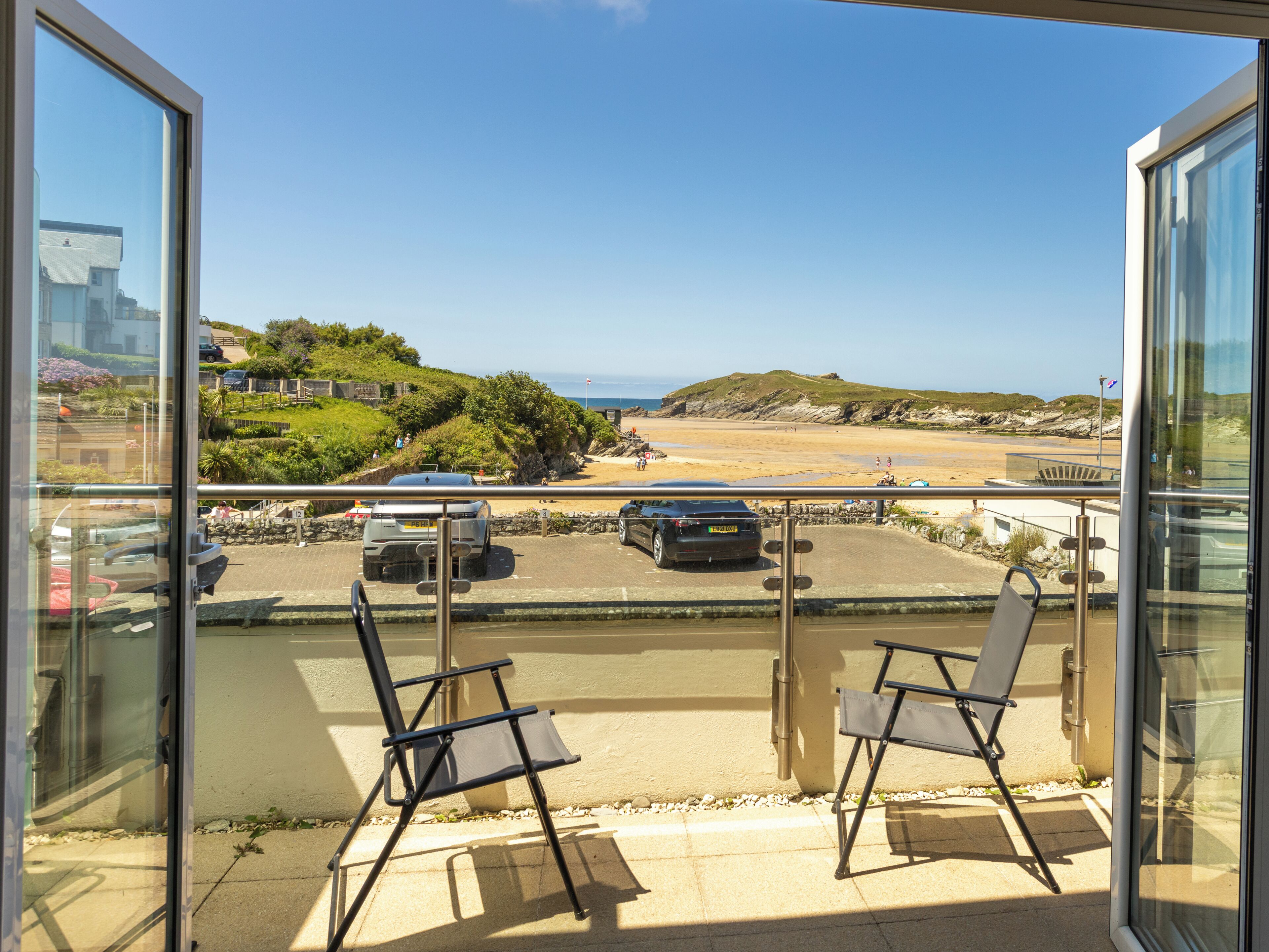 A balcony with two chairs overlooking a parking area and a beach.