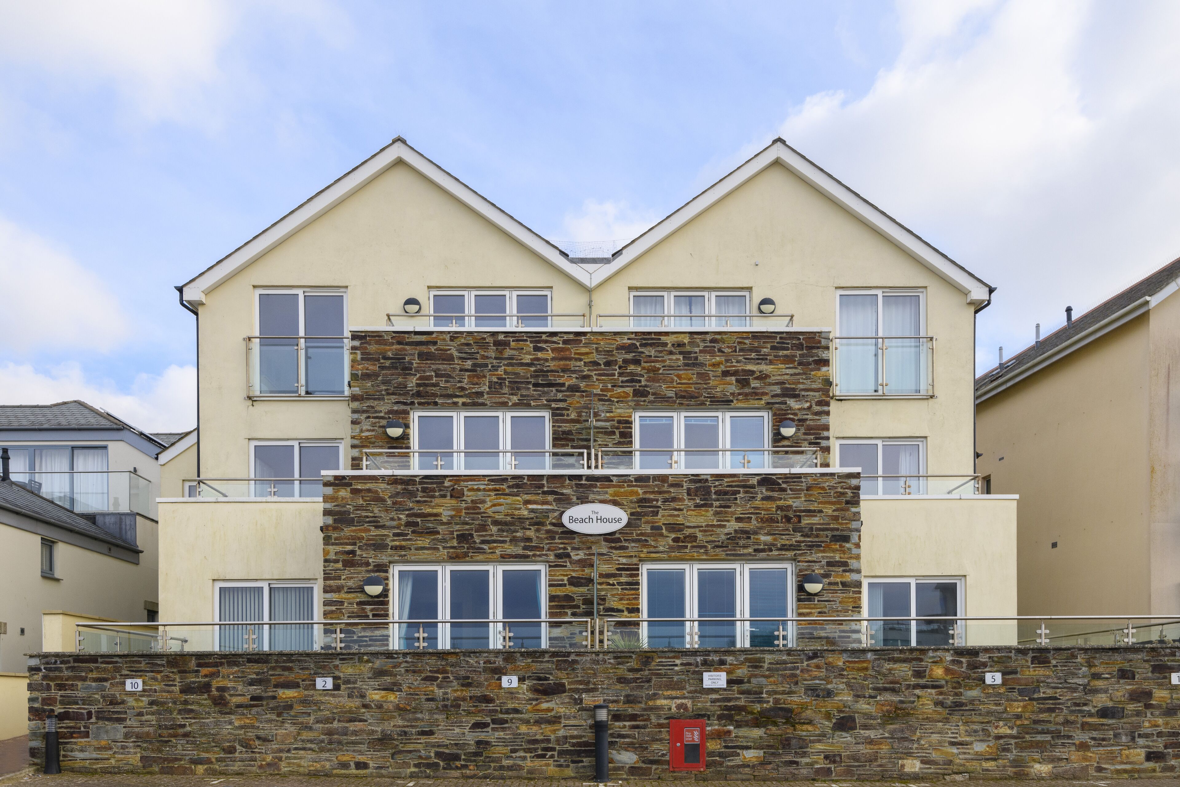 A multi-story building with a stone facade, multiple balconies, and a sign indicating "The Beach House."