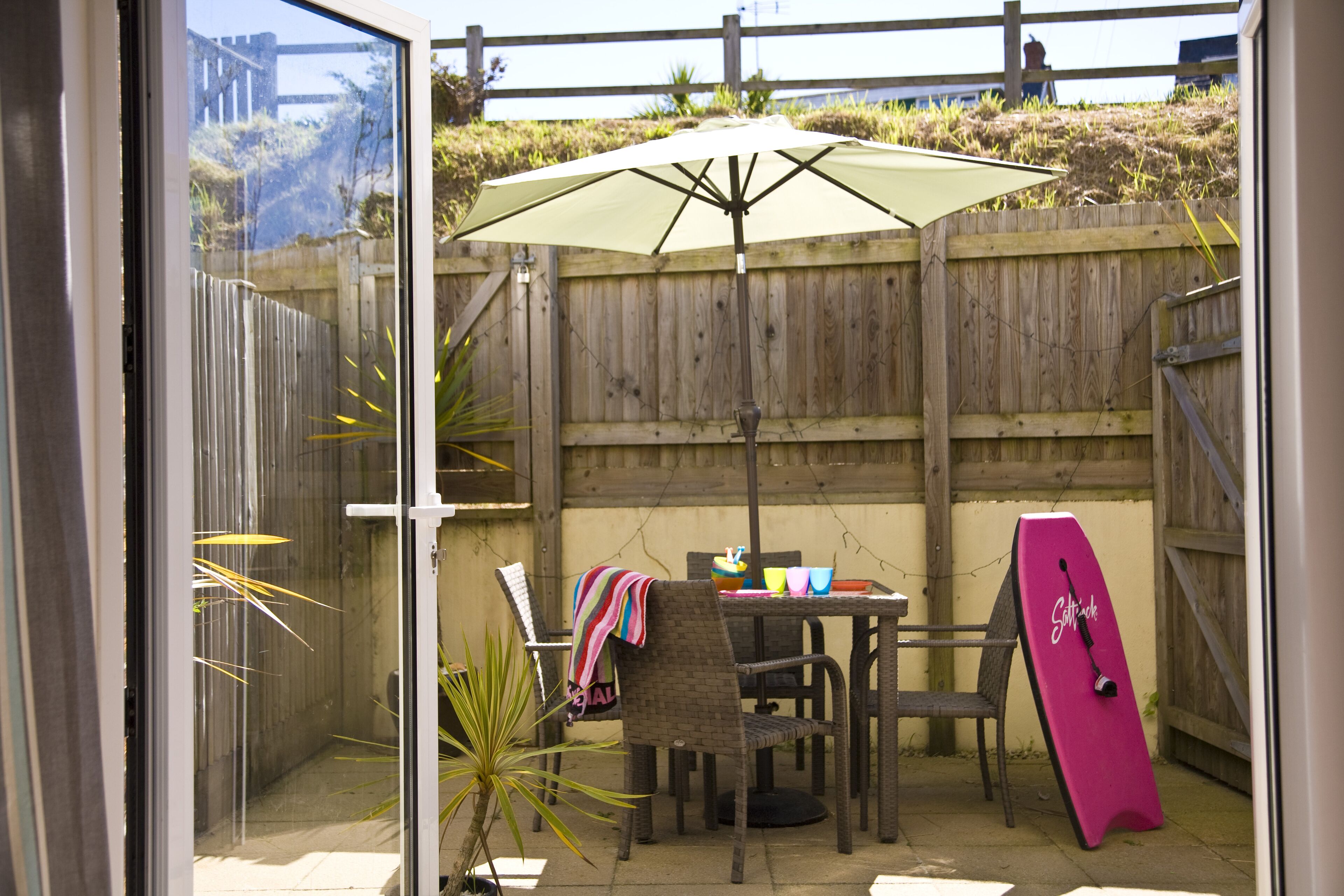 A patio area with a table, chairs, a surfboard, and an umbrella.