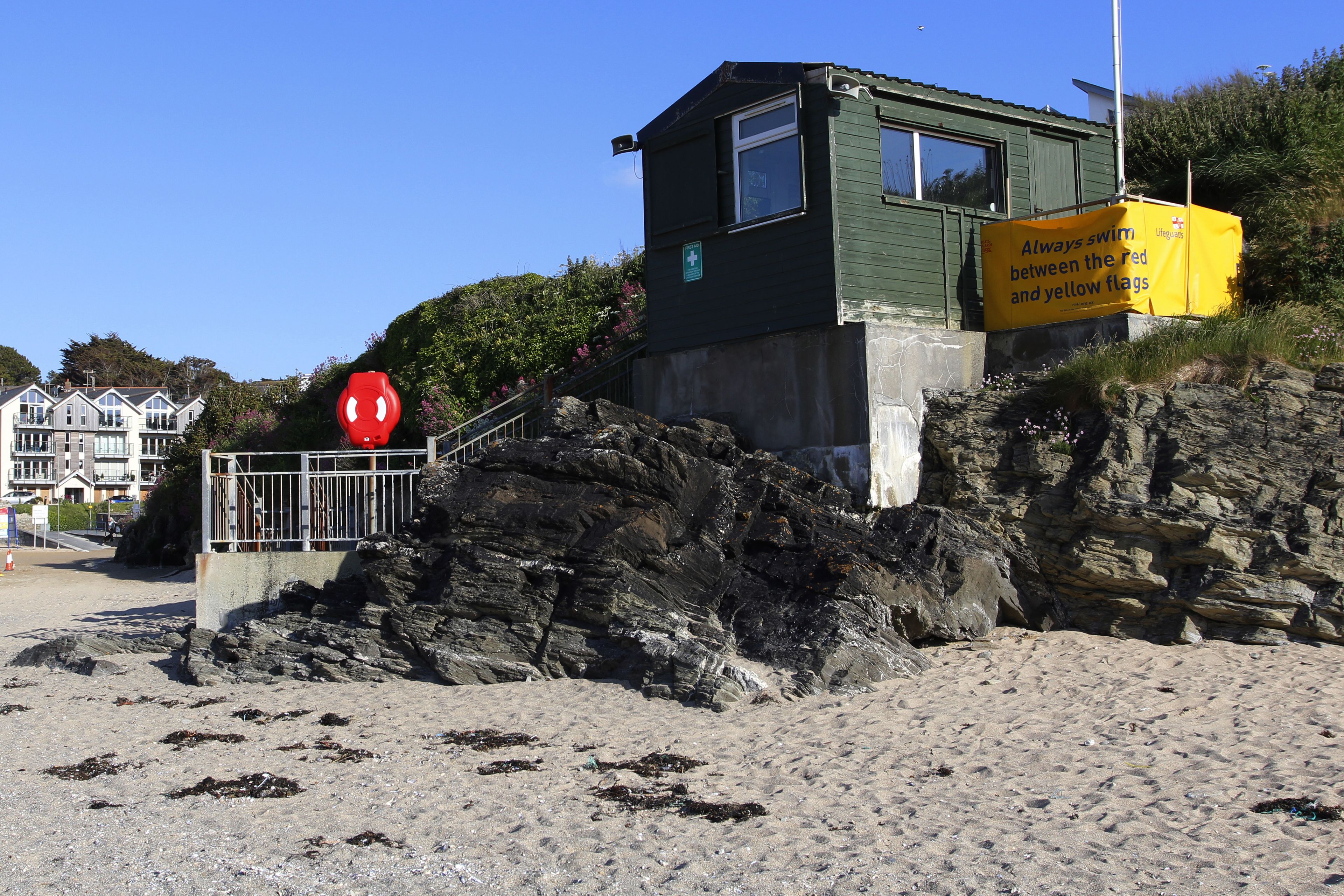 Et vagttårn for livreddere med et gult sikkerhedsskilte, placeret på en stenstrand med frit overblik over havet.