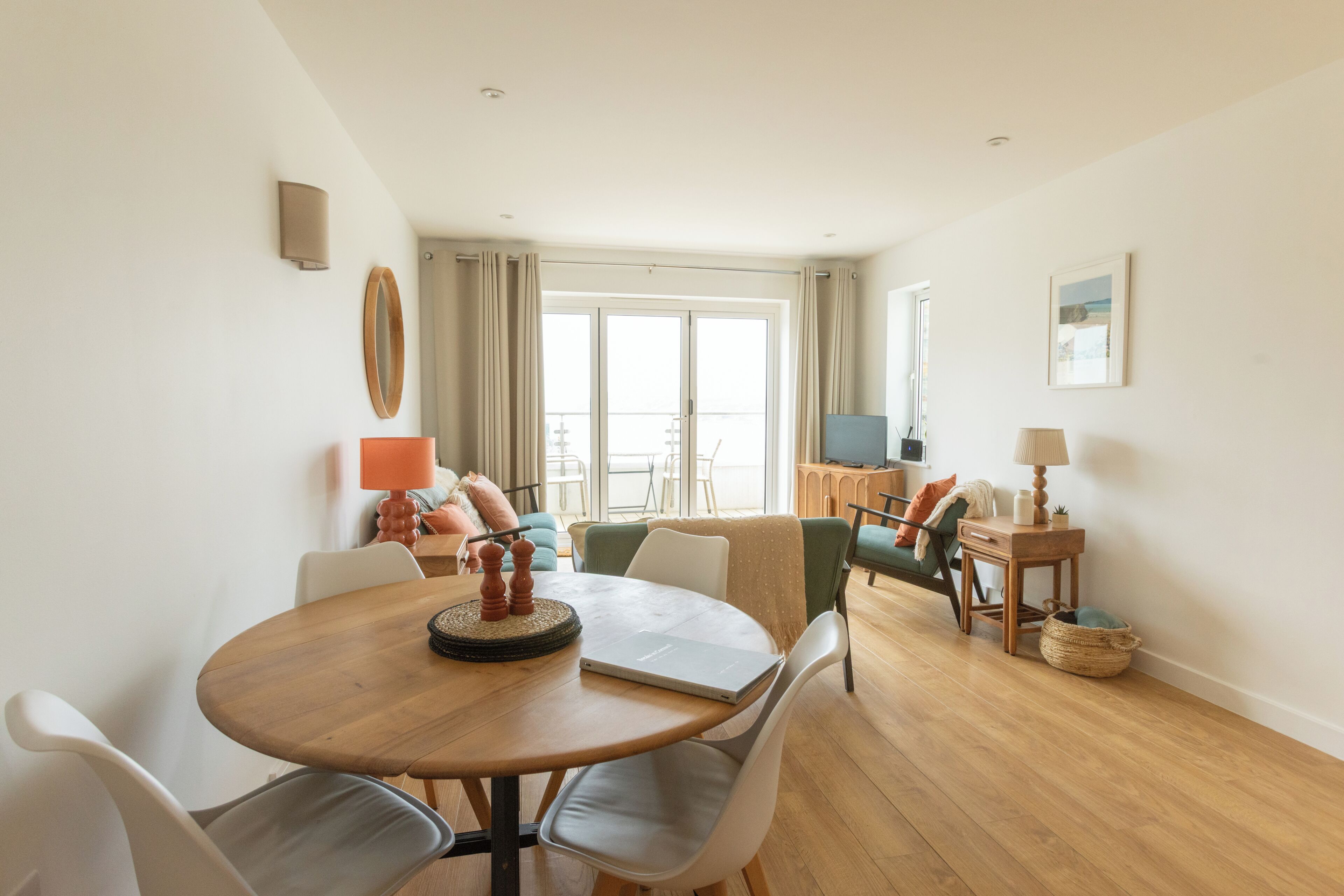 Una sala de estar moderna con una mesa redonda de madera, sillas blancas, un sofá y un televisor.