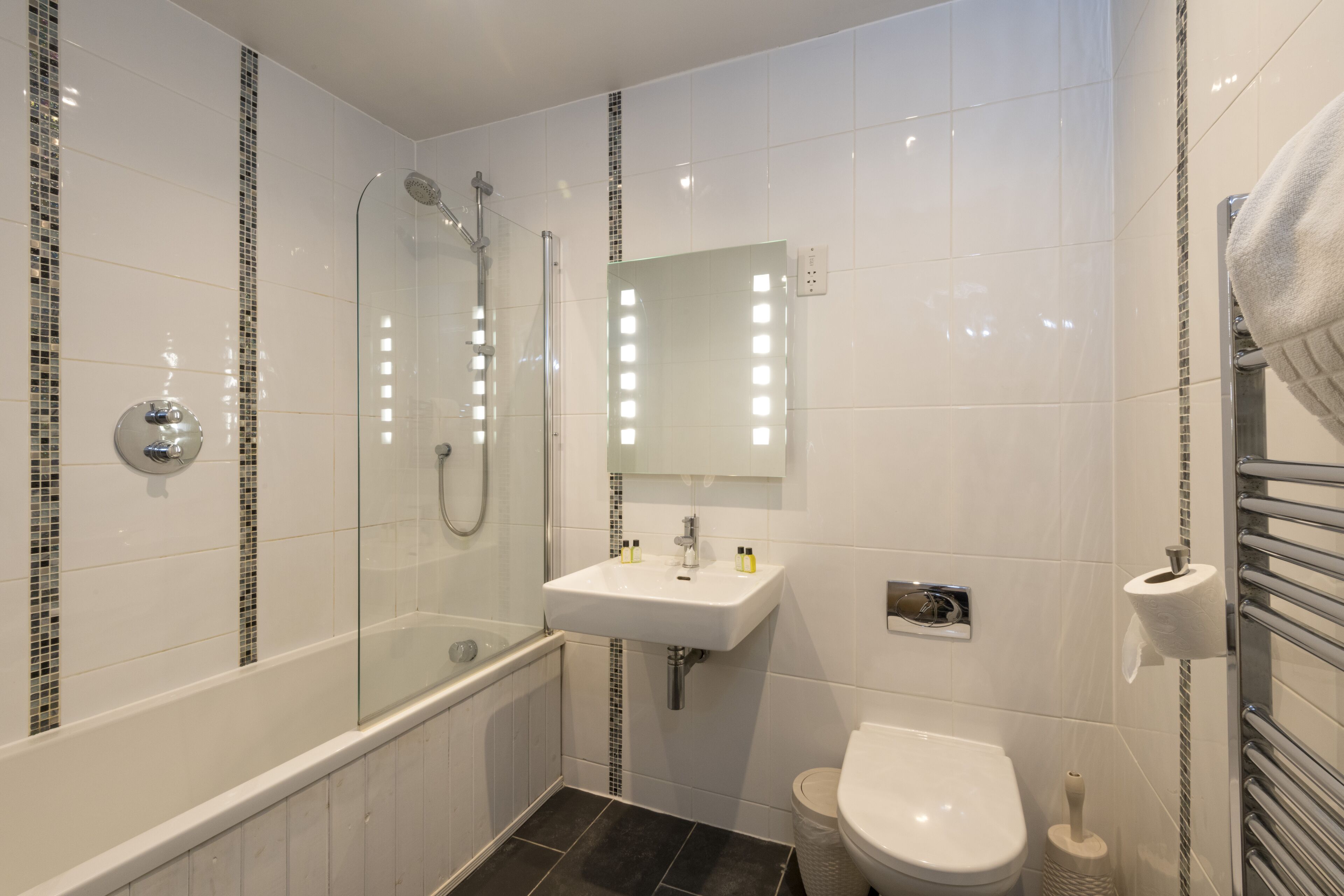 A modern bathroom with a glass-enclosed shower, a white sink with a mirror above it, and a toilet.