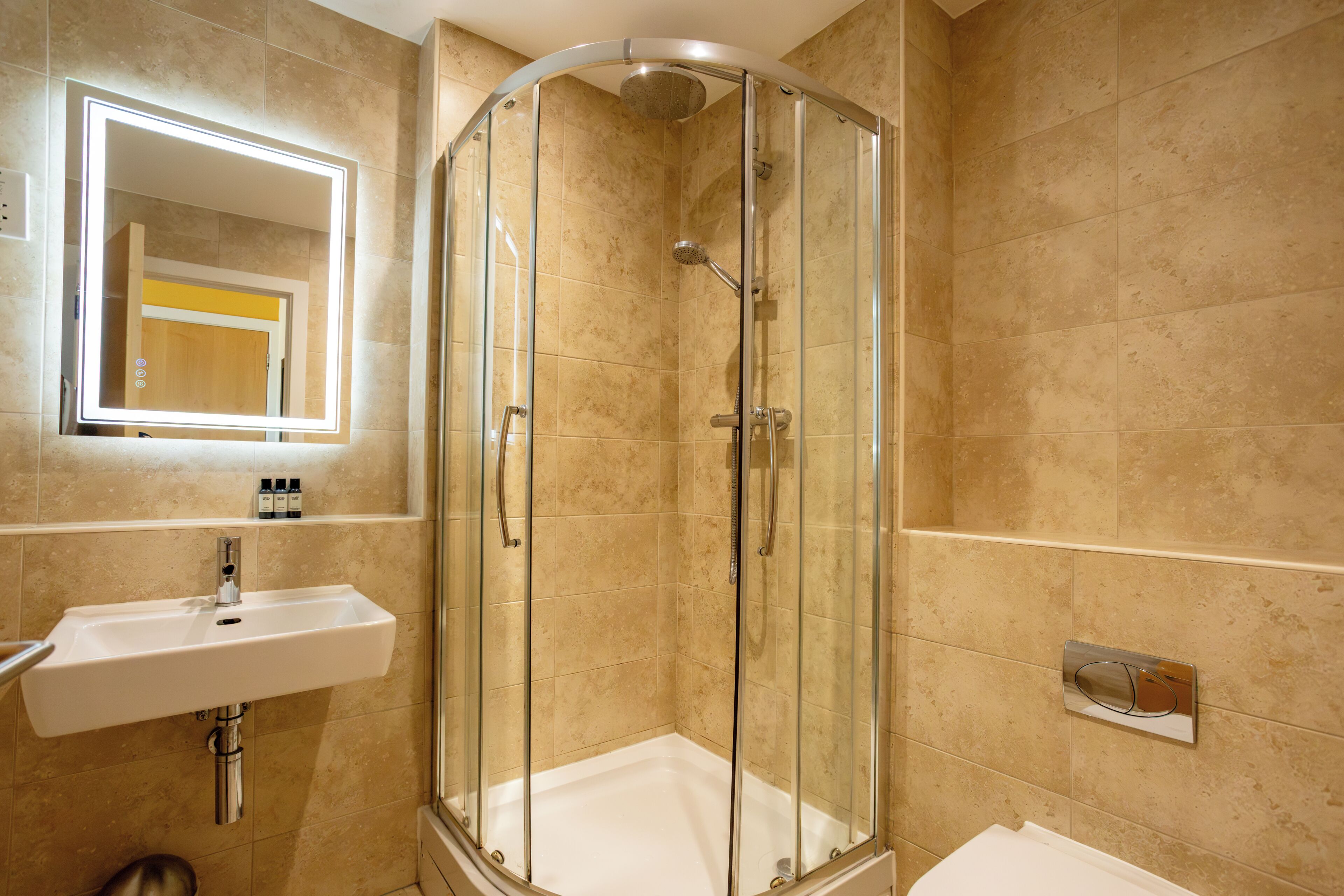 Un baño moderno con ducha envuelta en vidrio, lavamanos y espejo.