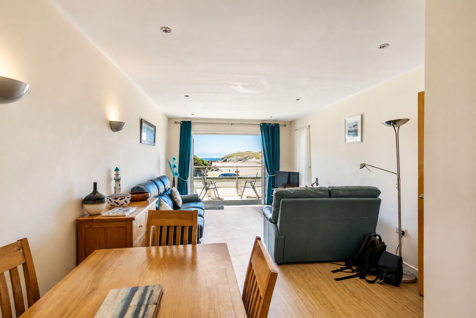 Ein Zimmer mit Esstisch, Stühlen, einer Couch, einem Fernseher und Blick auf den Strand.