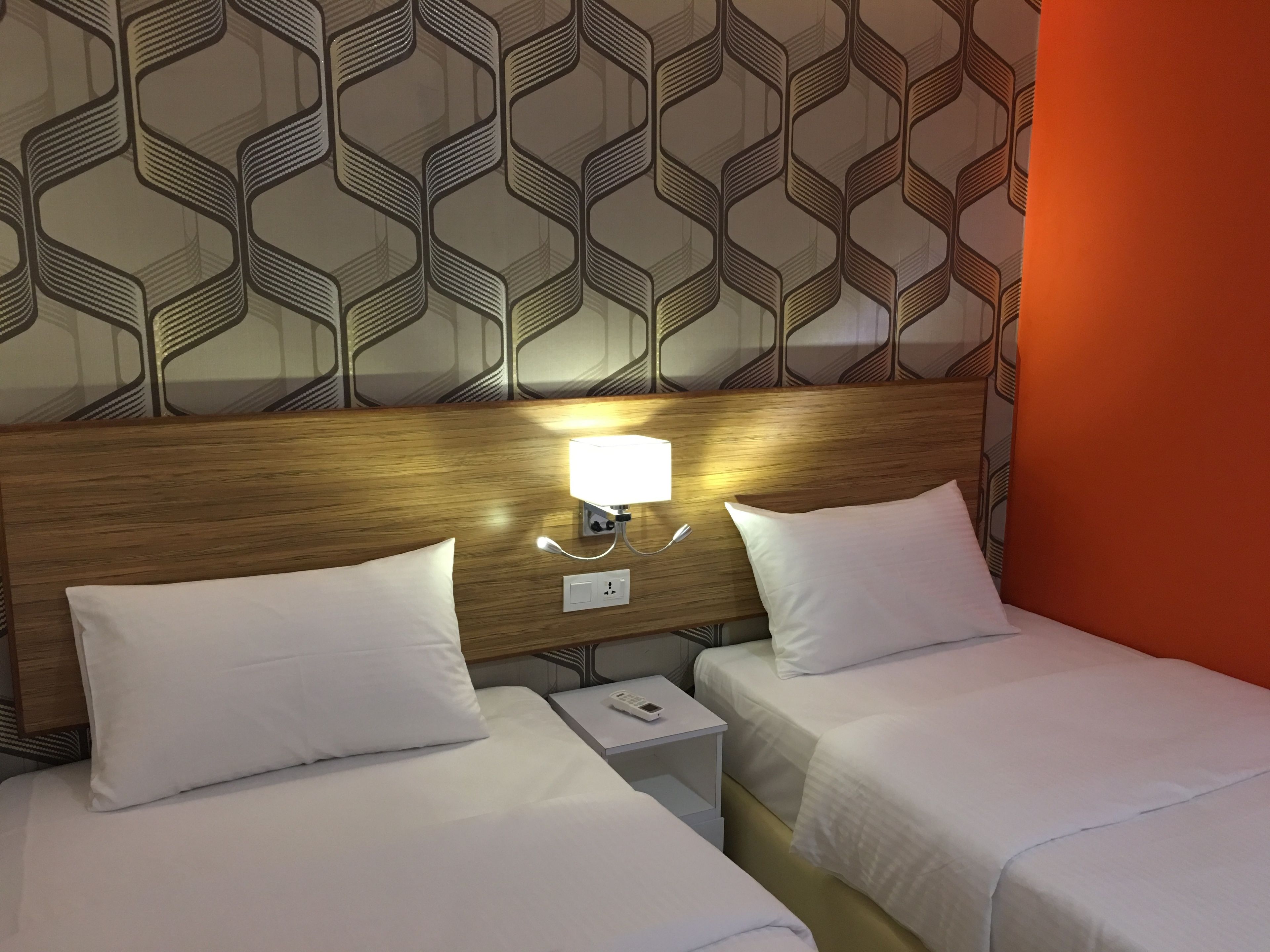 Camera d'albergo con due letti, una testiera in legno, un comodino con una lampada e una parete decorata.