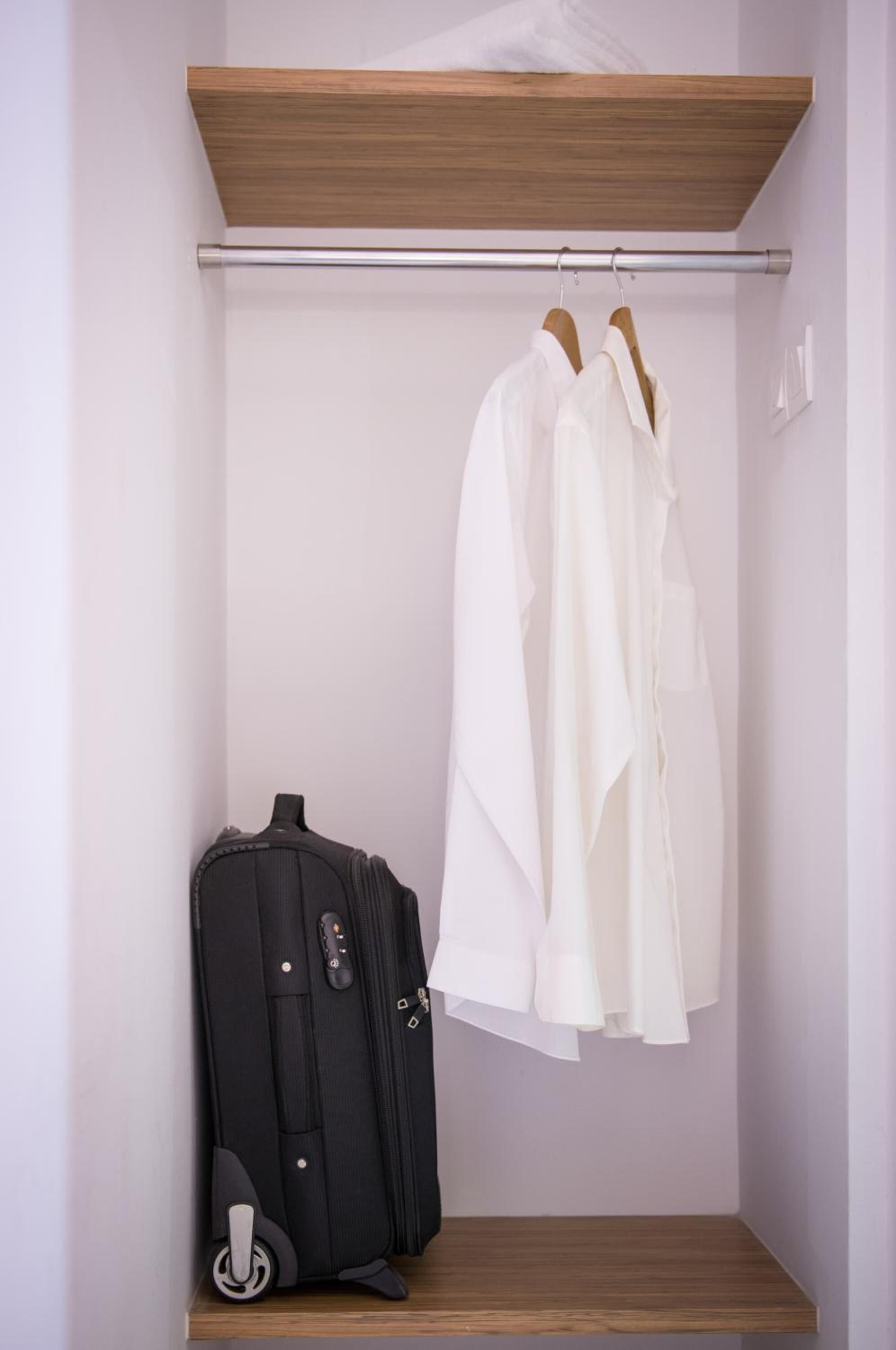 A closet with a wooden shelf, a hanging rod, and a suitcase.