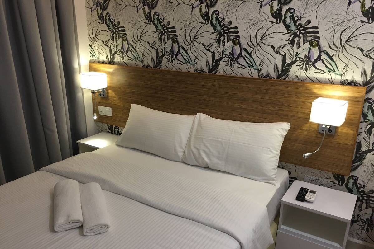A neatly made bed with white linens, two bedside lamps, and a nightstand with a remote control.