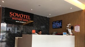 Uma receção de hotel com parede de mármore, um ecrã de televisão e um certificado na parede.