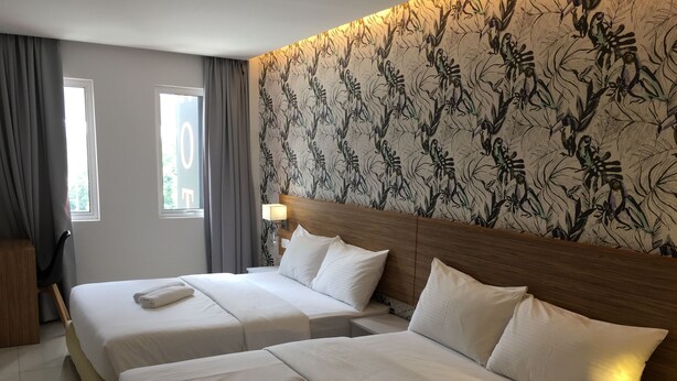 Quarto de hotel com duas camas, cabeceira de madeira, papel de parede estampado e janela com cortinas.