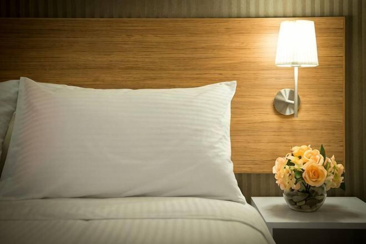 A neatly made bed with a pillow, a bedside lamp, and a vase with flowers on a nightstand.
