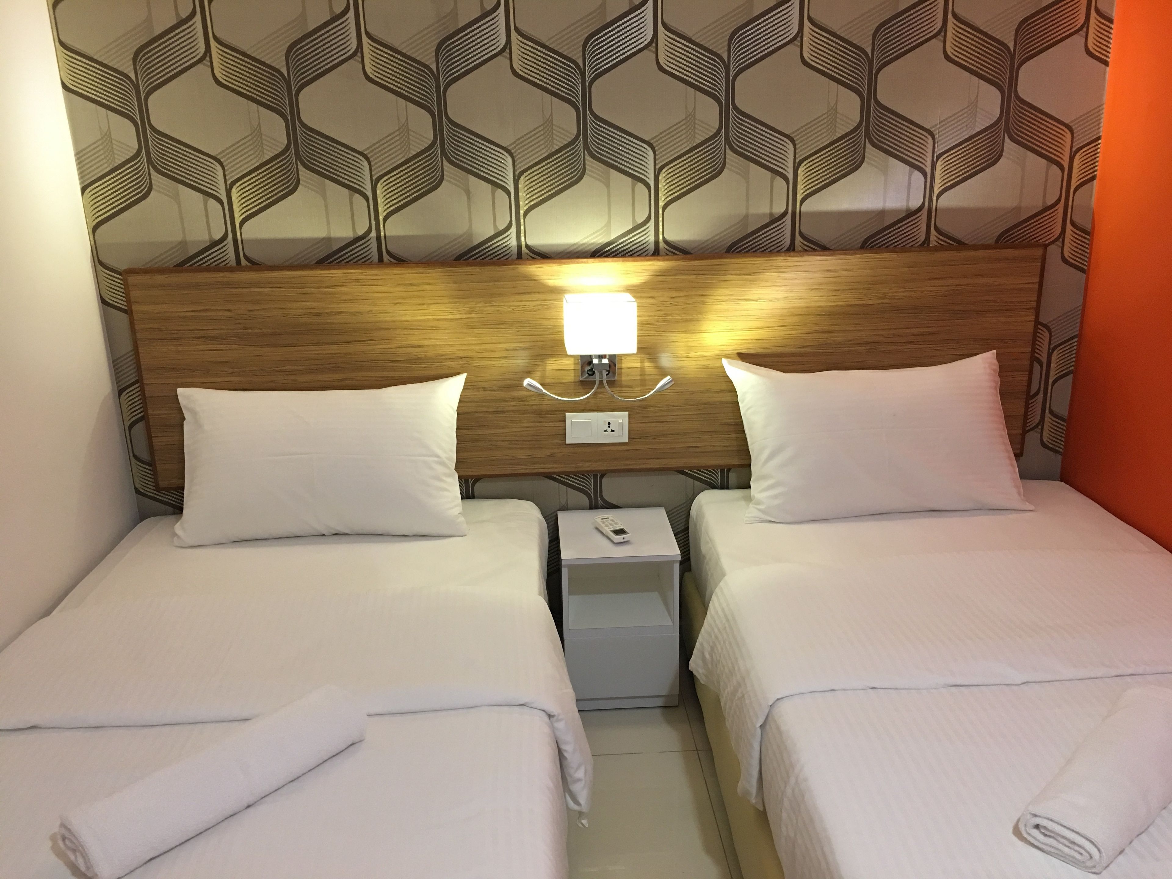 Une chambre d’h ôtel avec deux lits, une table de chevet, une lampe fixée au mur et un papier peint à motifs.