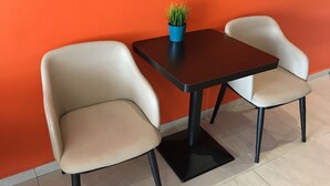 Uma pequena mesa com duas cadeiras, um vaso de planta e uma parede laranja.