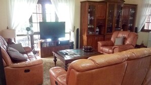 A living room with a brown leather sofa, a wooden cabinet, and a television. - Norfolk Heritage Airport Villa (Seeduwa - Katunayake)
