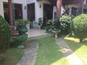 A courtyard with a stone pathway, potted plants, and a building with wooden doors and windows. - Norfolk Heritage Airport Villa (Seeduwa - Katunayake)