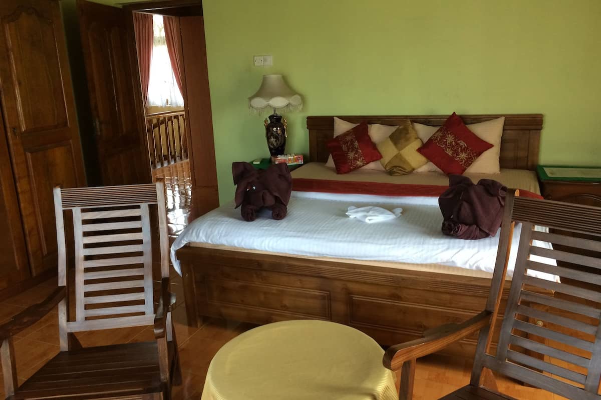 A room with a wooden bed, a nightstand, a lamp, and two wooden chairs.