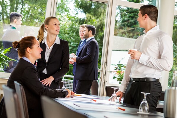 A business meeting in a modern office with large windows, a glass table, and a view of greenery outside.