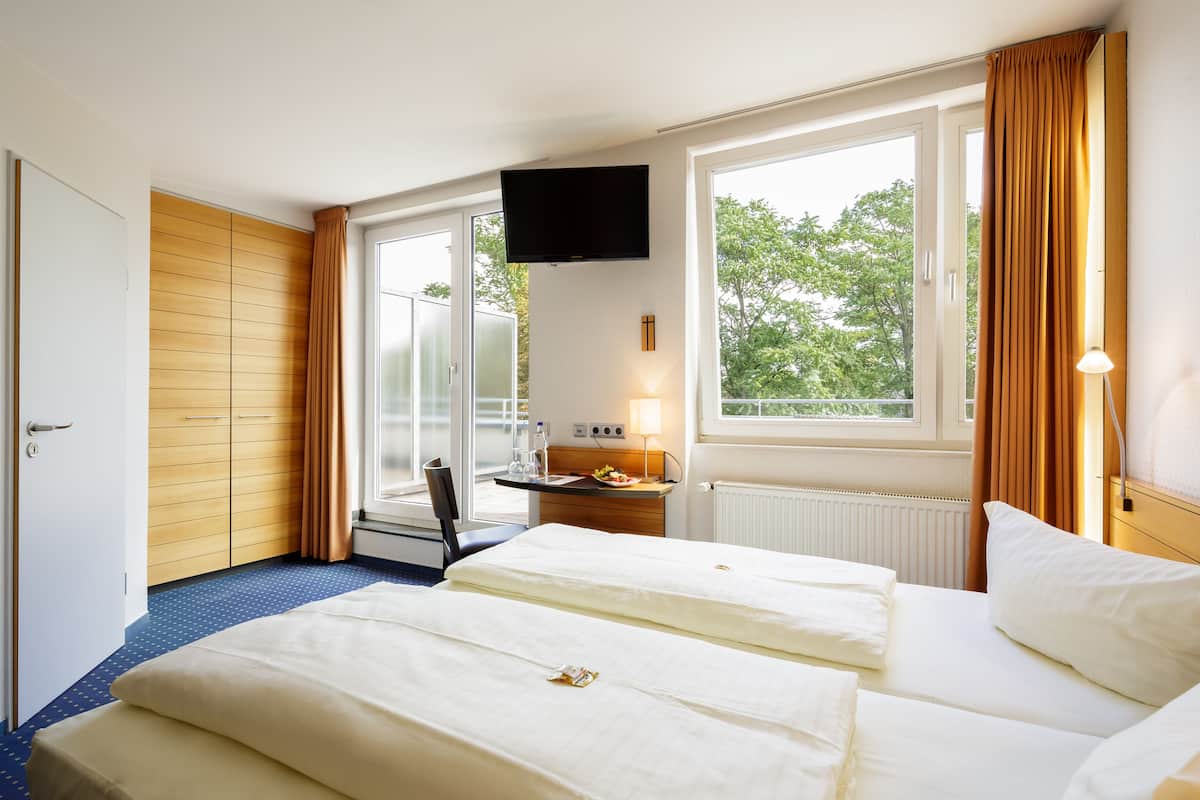 A hotel room with two beds, a desk with a chair, a TV, and large windows with curtains.