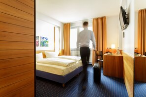 A hotel room with a bed, a desk, a chair, and a TV mounted on the wall.