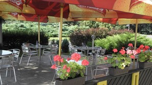 An outdoor seating area with tables and chairs under umbrellas, surrounded by greenery and potted plants. - Hotel Milotel (Olomouc)