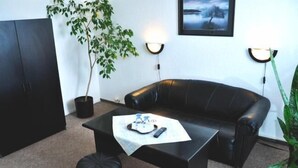 A living room with a black leather sofa, two black ottomans, a black coffee table with a remote control and a magazine, and two wall-mounted lamps. - Hotel Milotel (Olomouc)