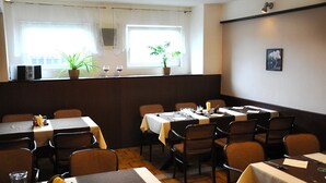 A restaurant with multiple tables and chairs, a potted plant, and a window with curtains. - Hotel Milotel (Olomouc)