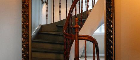 A mirror with an ornate frame reflecting a staircase with wooden balusters and a handrail.