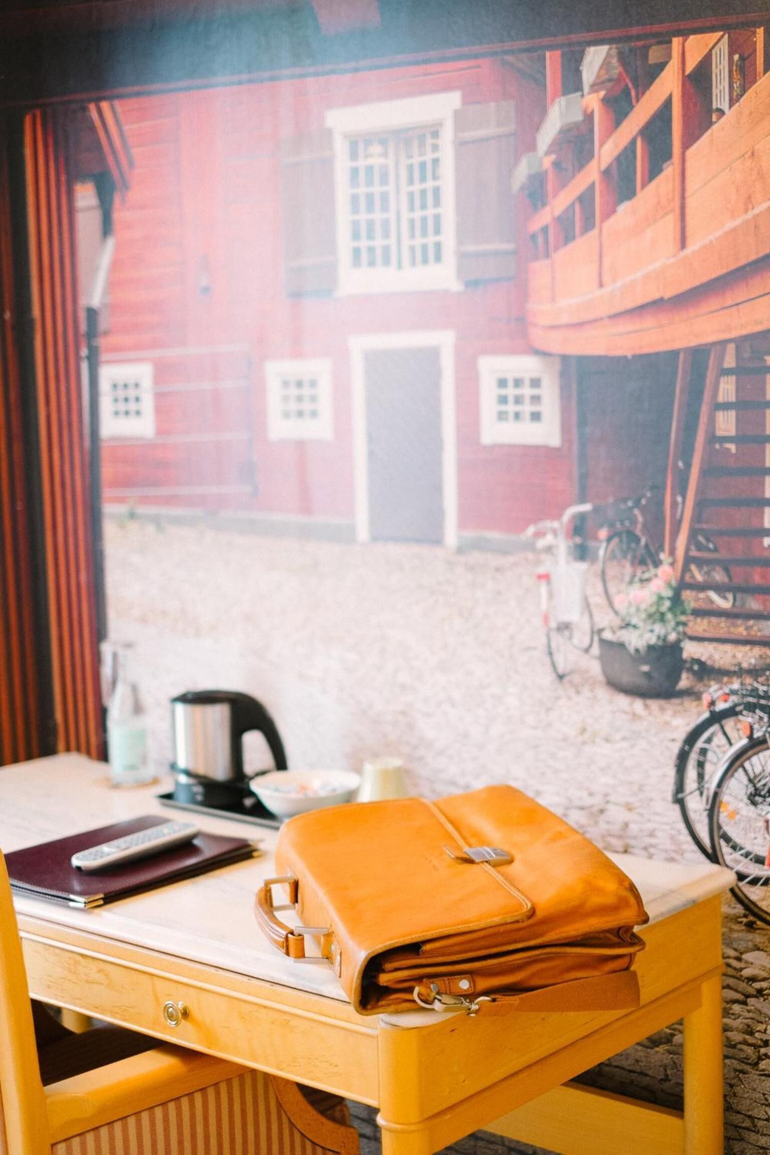 A wooden desk with a yellow bag, a notebook, and a pen.