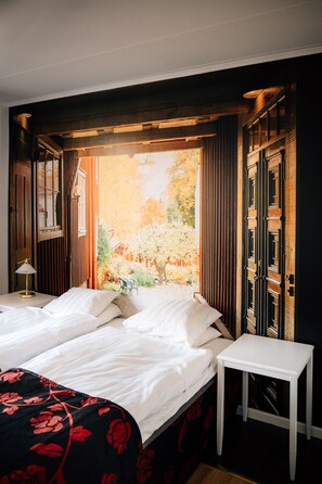 Un dormitorio con una cama grande, una mesita de noche y vistas a un jardín por la ventana.