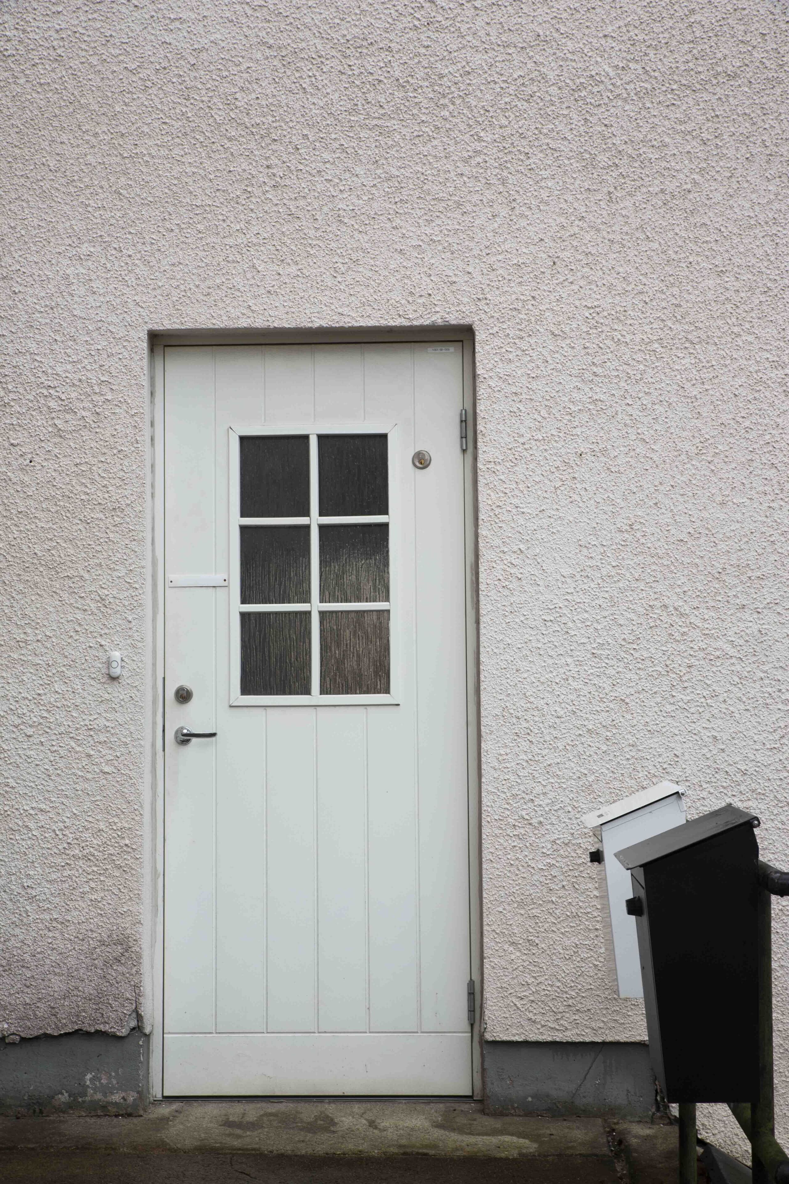 A white door with a window, a small mailbox, and a textured wall.