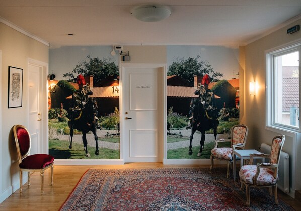 A room with a large mural of a horse and rider, a red chair, a patterned rug, and a white door with a nameplate. - Eksjö Stadshotell Annex (Eksjo)