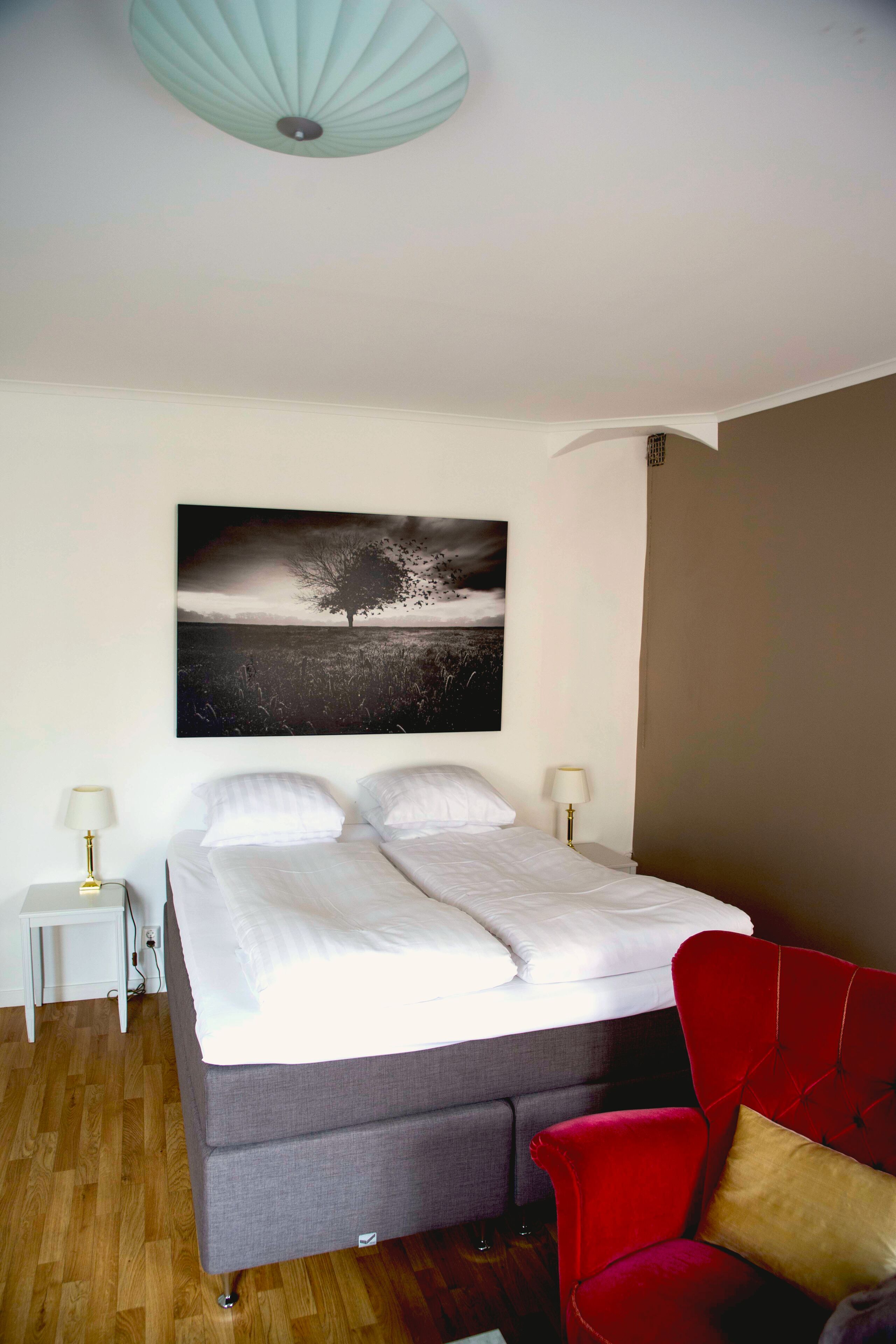 Un dormitorio con una cama, una silla roja, una mesita de noche y una lámpara de pared.