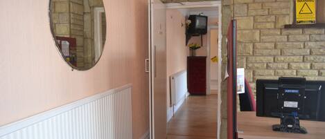 A hallway with a mirror, a radiator, a warning sign, and a television on the wall.