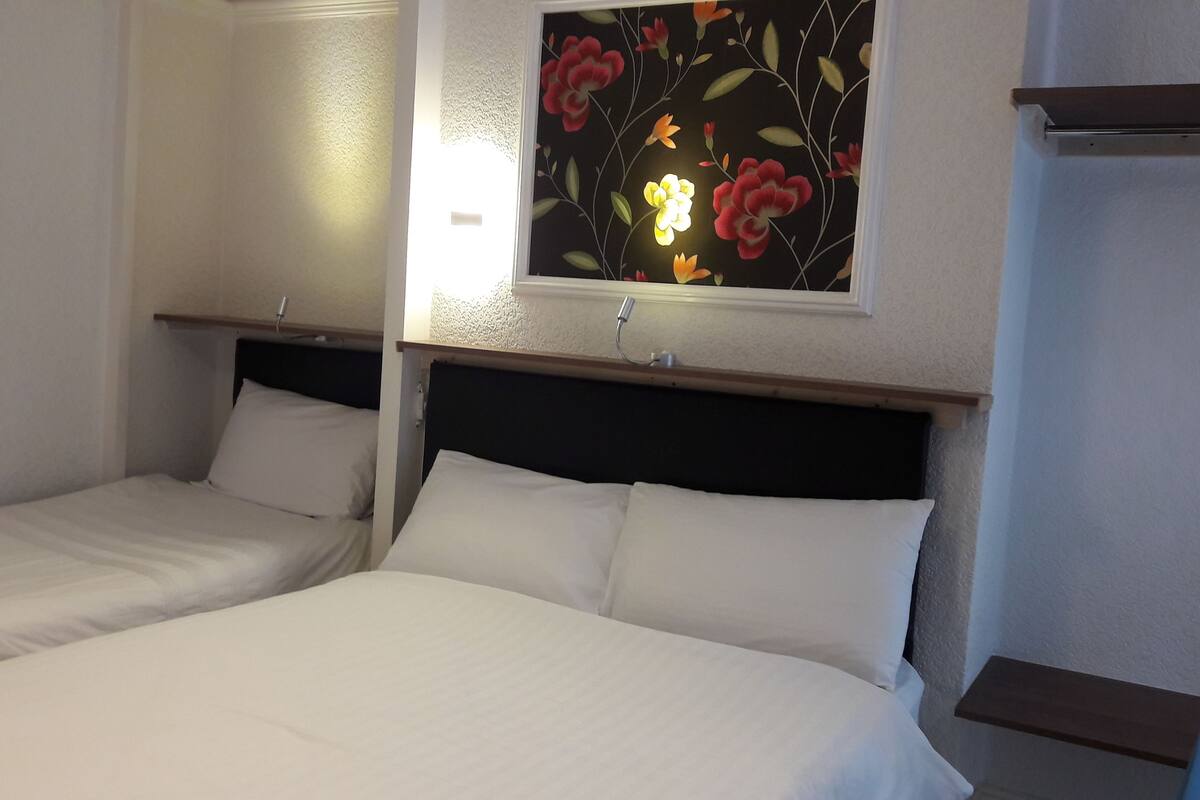 Two single beds with white linens, a dark headboard, and a floral wall decoration.
