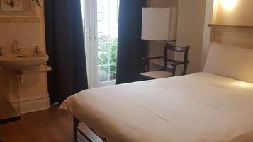 Une chambre d’hôtel comprenant un lit, une table de chevet, une chaise, une fenêtre avec des rideaux, un lavabo et un miroir.