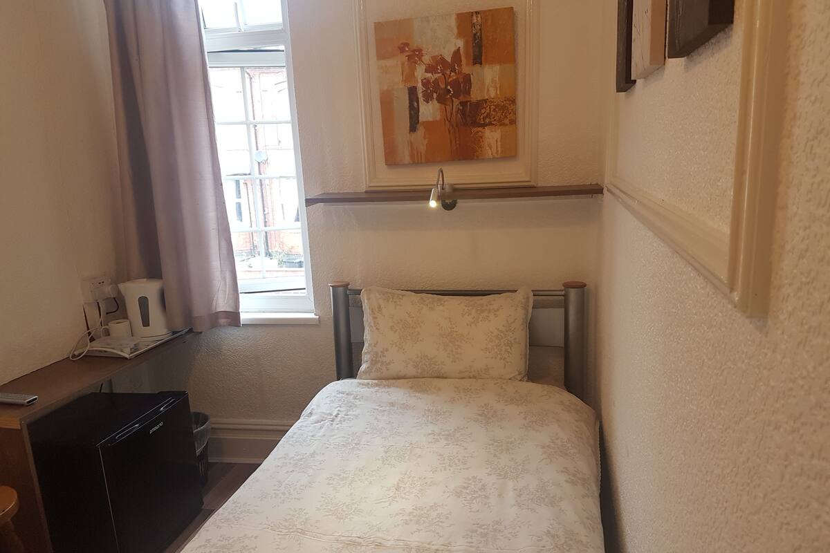 A bedroom with a bed, a desk, a chair, a window with curtains, and a painting on the wall.
