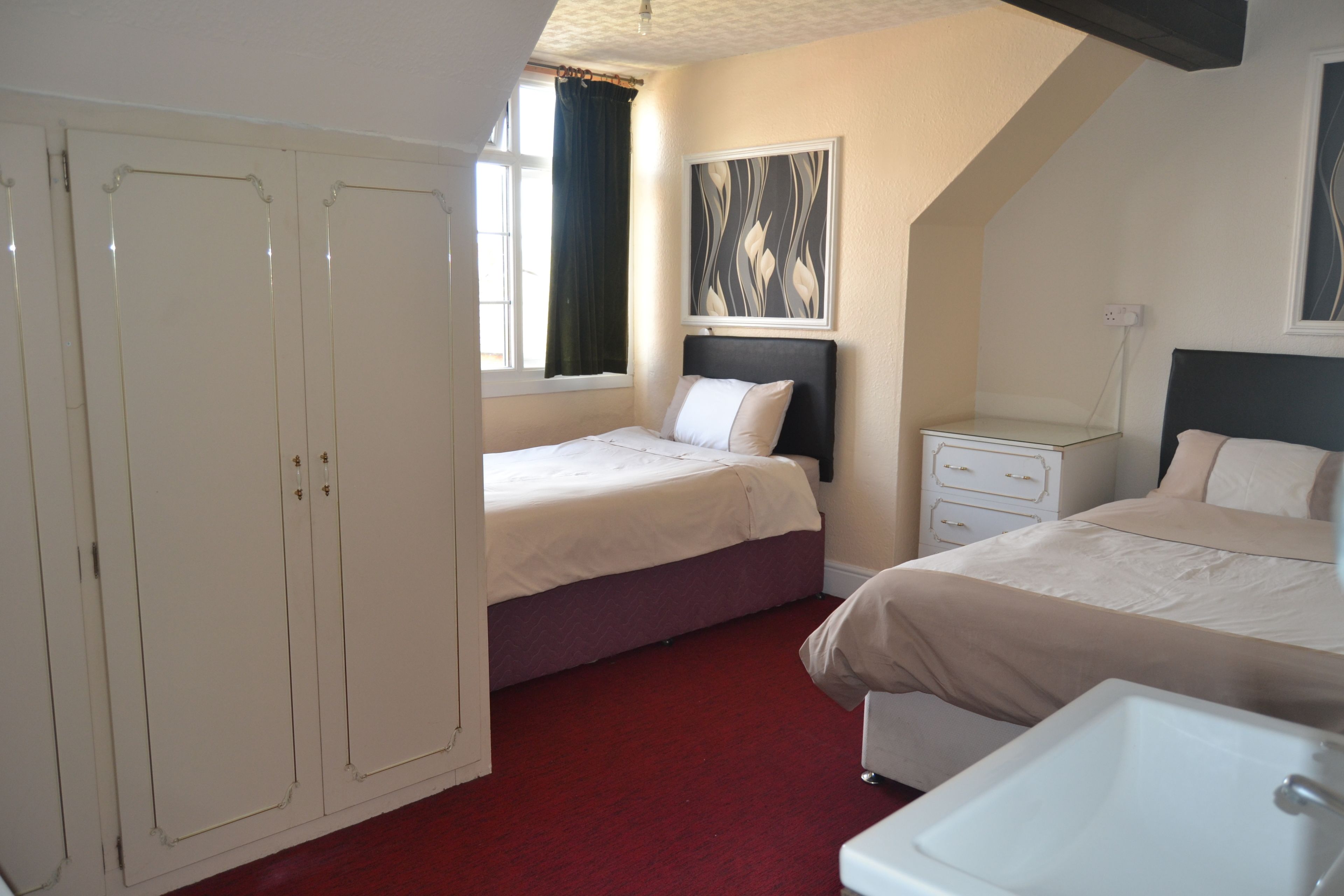 A bedroom with two beds, a wardrobe, a bedside table, a nightstand, and a painting on the wall.