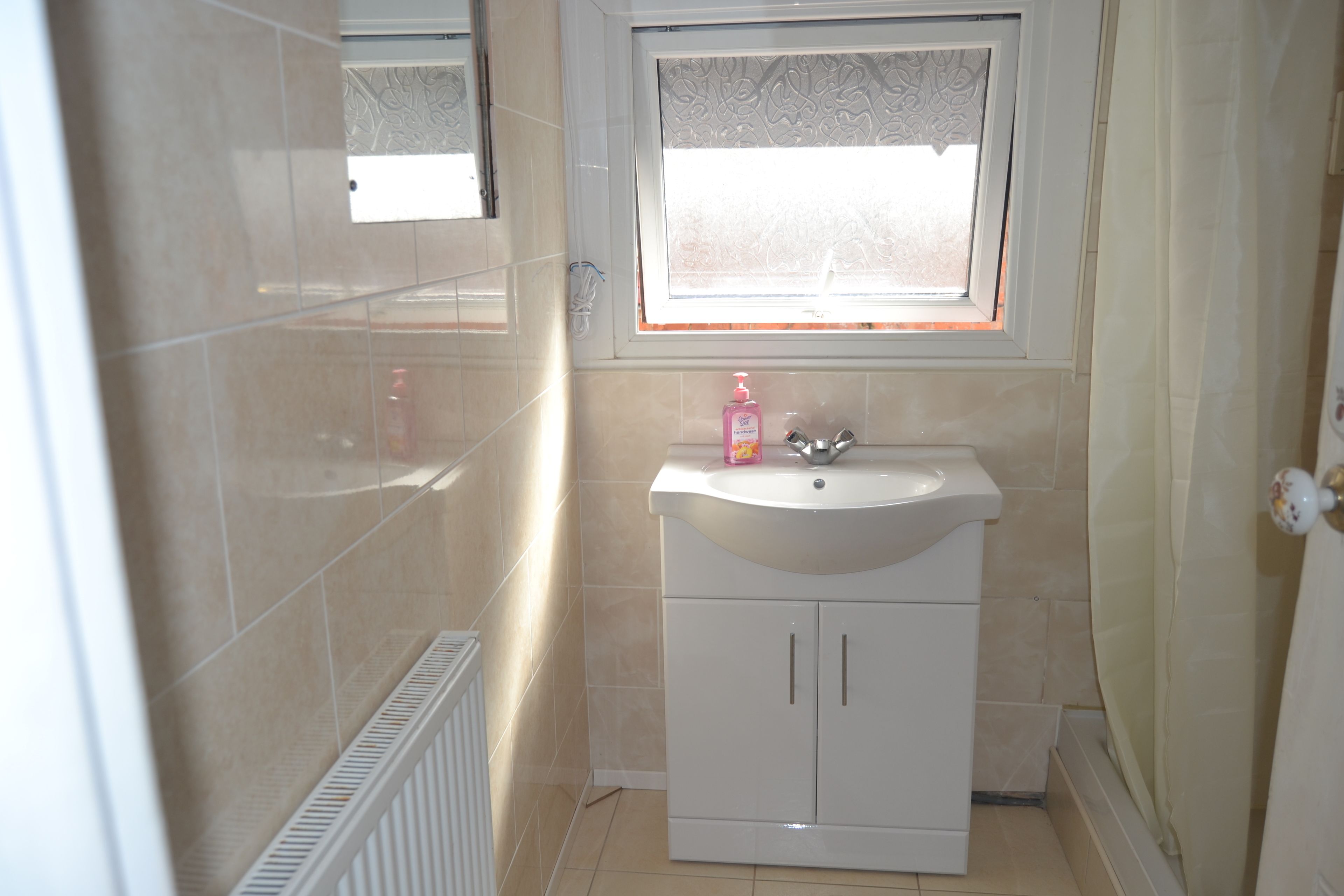 A small bathroom with a white sink, a mirror above it, and a window with a decorative pattern.