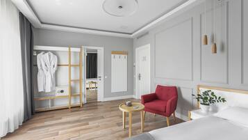 Una habitación de hotel moderna con suelo de madera, un sillón rojo, una cama, una mesita de noche con una planta y un armario con espejo.
