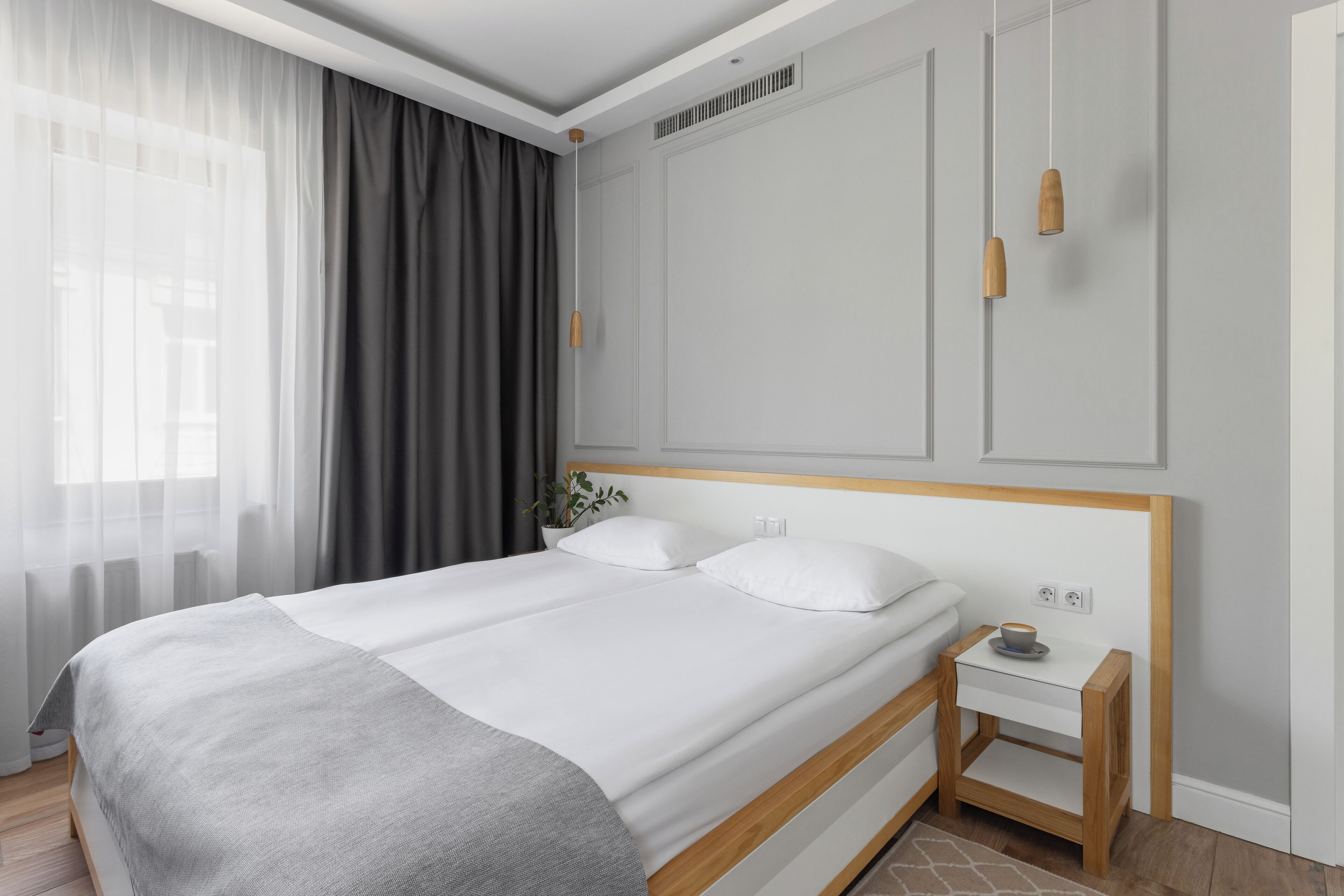 A modern bedroom with a large bed, a bedside table with a cup, and a window with sheer curtains.