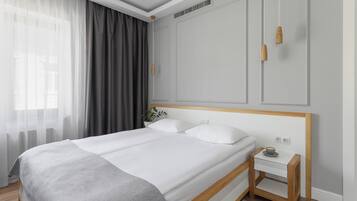 A modern bedroom with a large bed, a bedside table with a cup, and a window with sheer curtains.