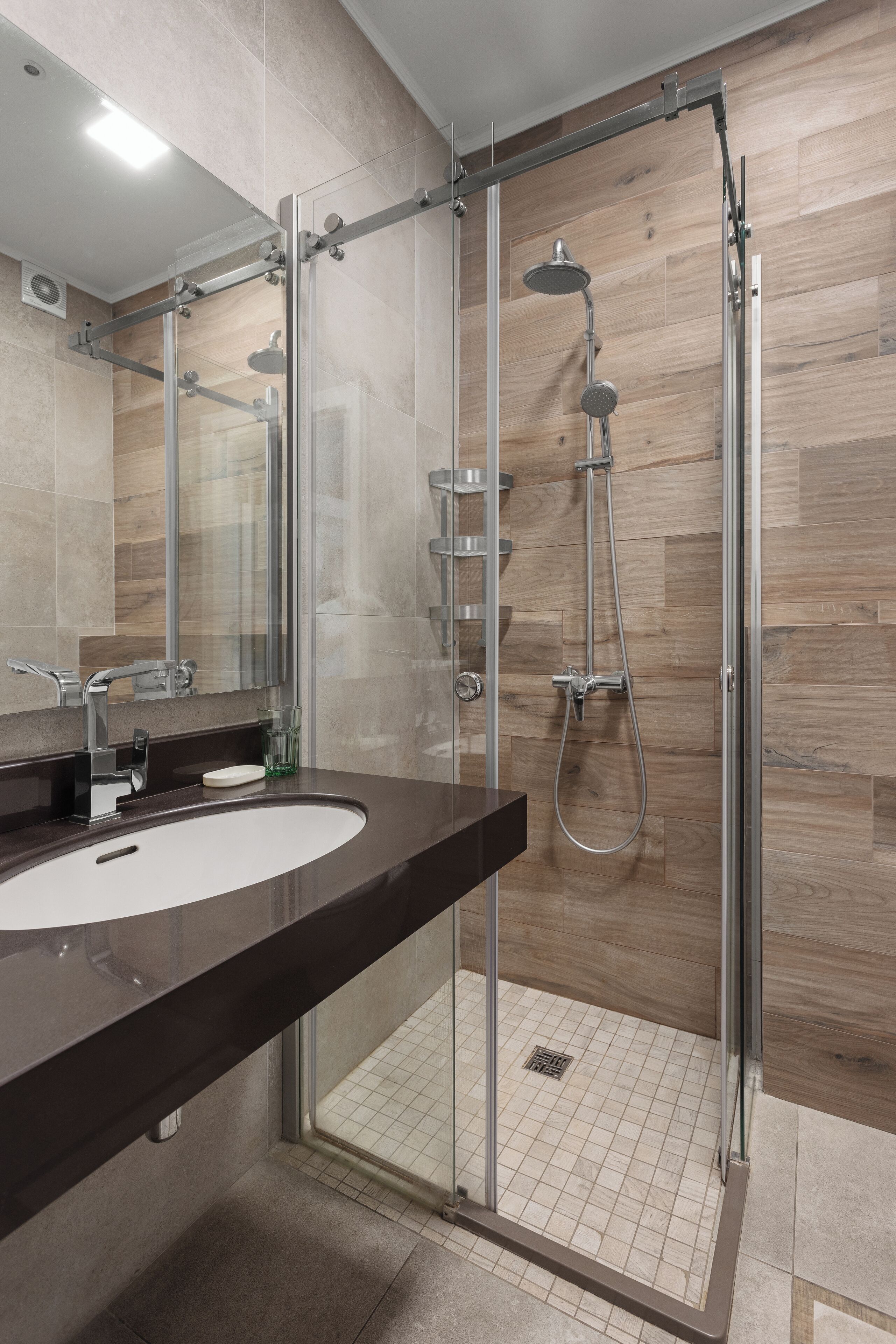 A modern bathroom with a glass-enclosed shower, a dark countertop sink, and a mirror.