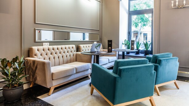 A modern lobby with a beige sofa, teal armchairs, a round table, and a large mirror. - Frapolli 21 (Odesa)